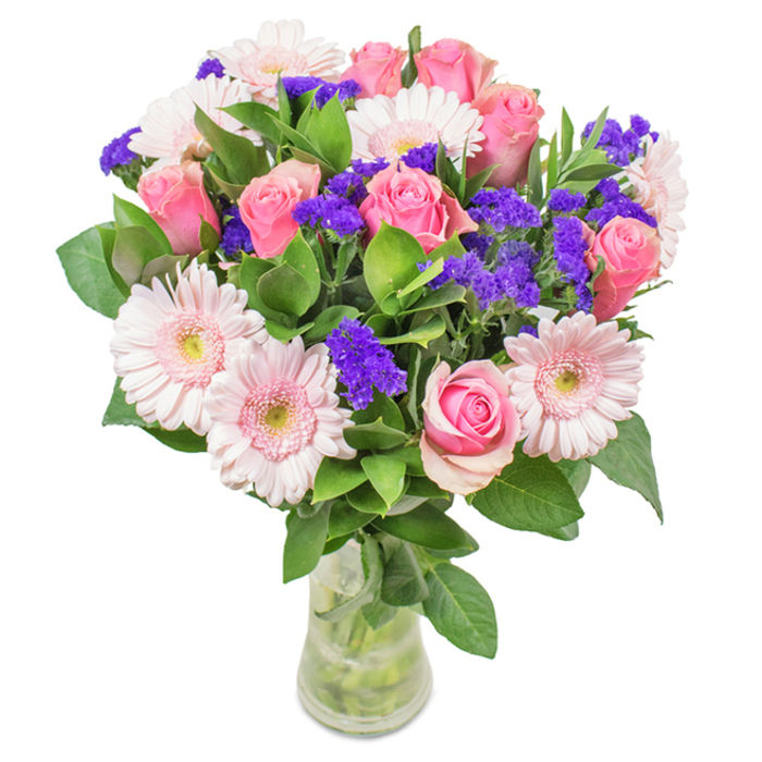 Seen against a crisp white background, this elegant arrangement-crafted by Flowers Barnsbury-features around eight pink roses, each petal softly furled or gently opening to reveal a timeless spiral heart. These roses are complemented by light pink gerbera daisies, distinguished by their bold, round faces and nearly white centres, all set amidst lively clusters of deep purple statice. The statice infuses the bouquet with texture and contrast, its papery petals a nod to wildflowers found in local parks like Barnsbury Wood. Beneath, plush green foliage provides a fresh, abundant base, its shades recalling the hidden gardens of Hemingford Road. Presented in a clear, slender glass vase where the stems twine elegantly in clean water, this arrangement embodies the artistry of local Barnsbury florists. Ideal as a generous gift for a birthday, anniversary, or Mother's Day, or as a beautiful accent for a shopfront or dining table, this bouquet channels feelings of joy and celebration while anchoring its beauty in Barnsbury's vibrant community.
